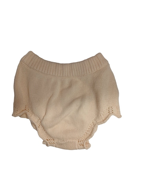 Beige knitted garment on a white surface with scissors and a calculator in the background.