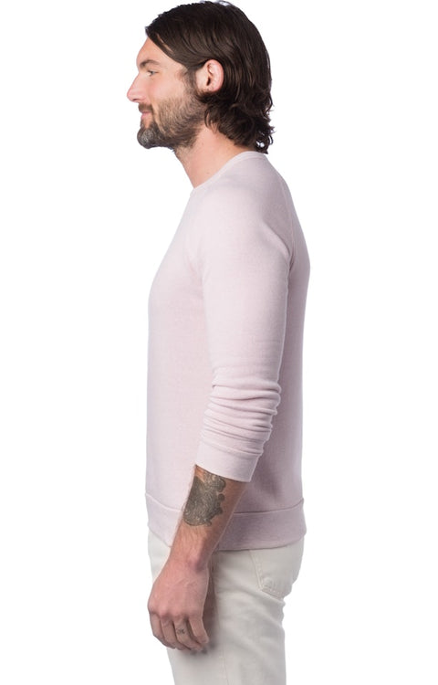 Man wearing a light pink sweater and white pants on a white background