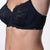 Close-up of a model wearing a black lace and mesh underwire bra against a light gray studio background.