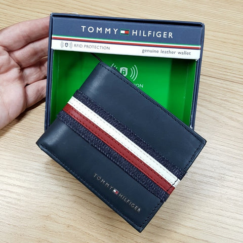 Tommy Hilfiger wallet with striped design held by a hand, displayed against a wooden surface.
