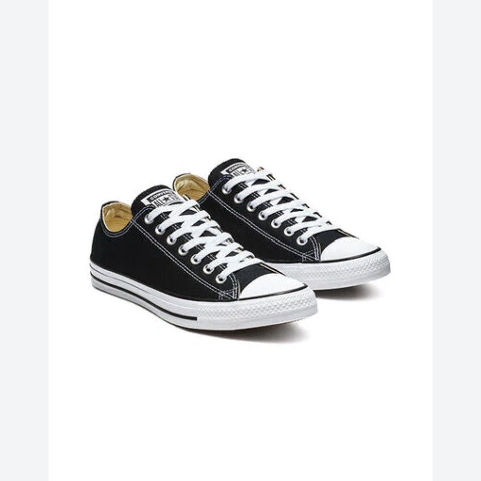 A pair of classic low-top canvas sneakers in black with white laces, white rubber toe caps and midsoles, and a tan interior lining, shown on a plain white background.