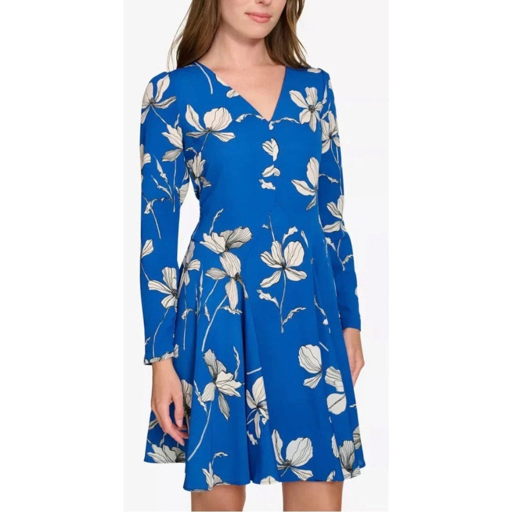 A woman wearing a bright blue long-sleeve V-neck dress with a white floral print, shown against a plain white background.