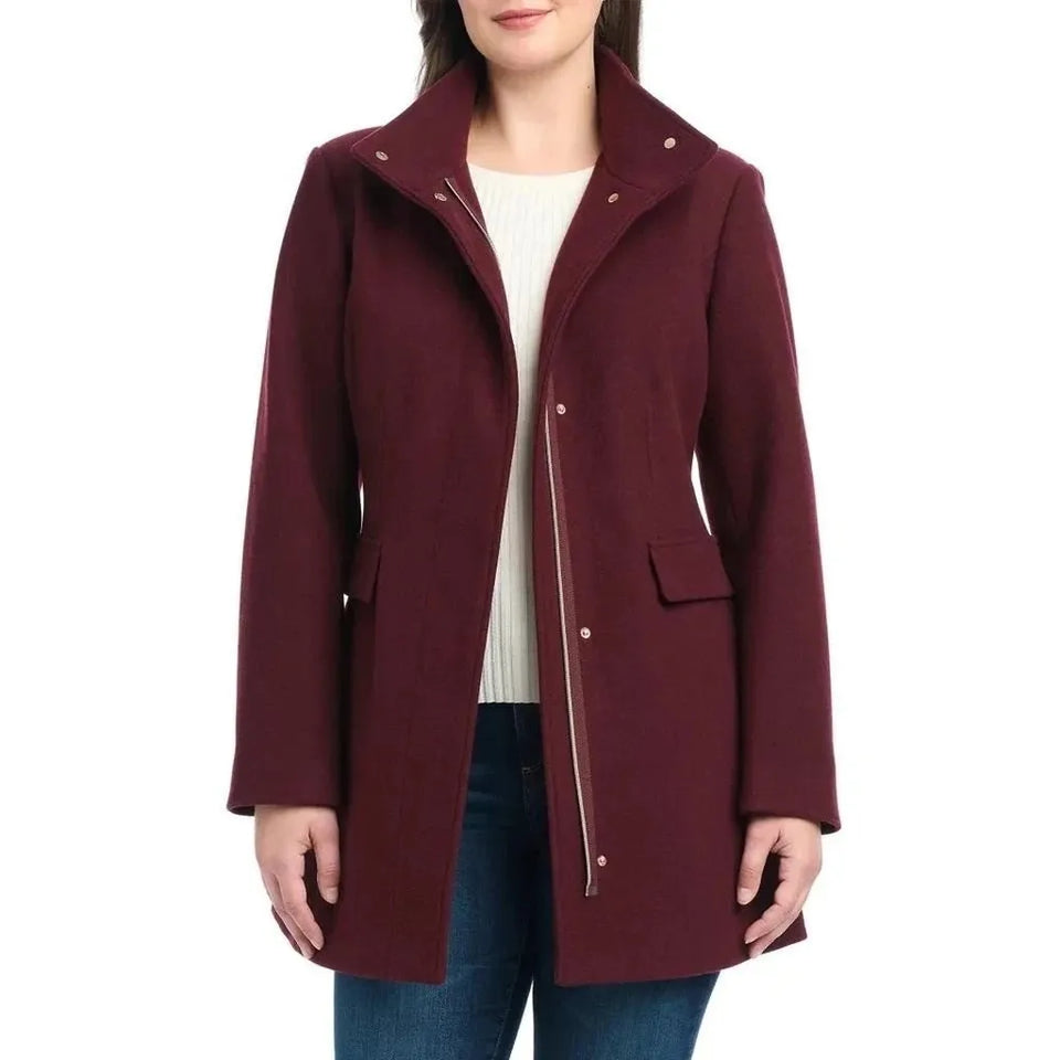 A woman wearing a burgundy wool-blend coat with a high collar, front zipper, and snap buttons, styled over a white top and blue jeans against a plain white background.