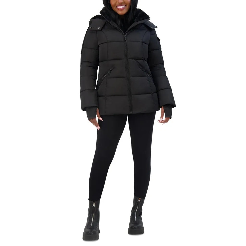 A woman modeling a black hooded puffer jacket with horizontal quilting, black leggings, and black ankle boots against a plain white background.