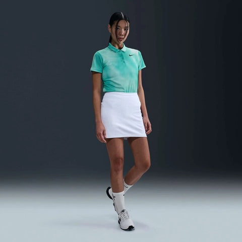 Woman wearing a green Nike polo shirt and white skirt on a dark background