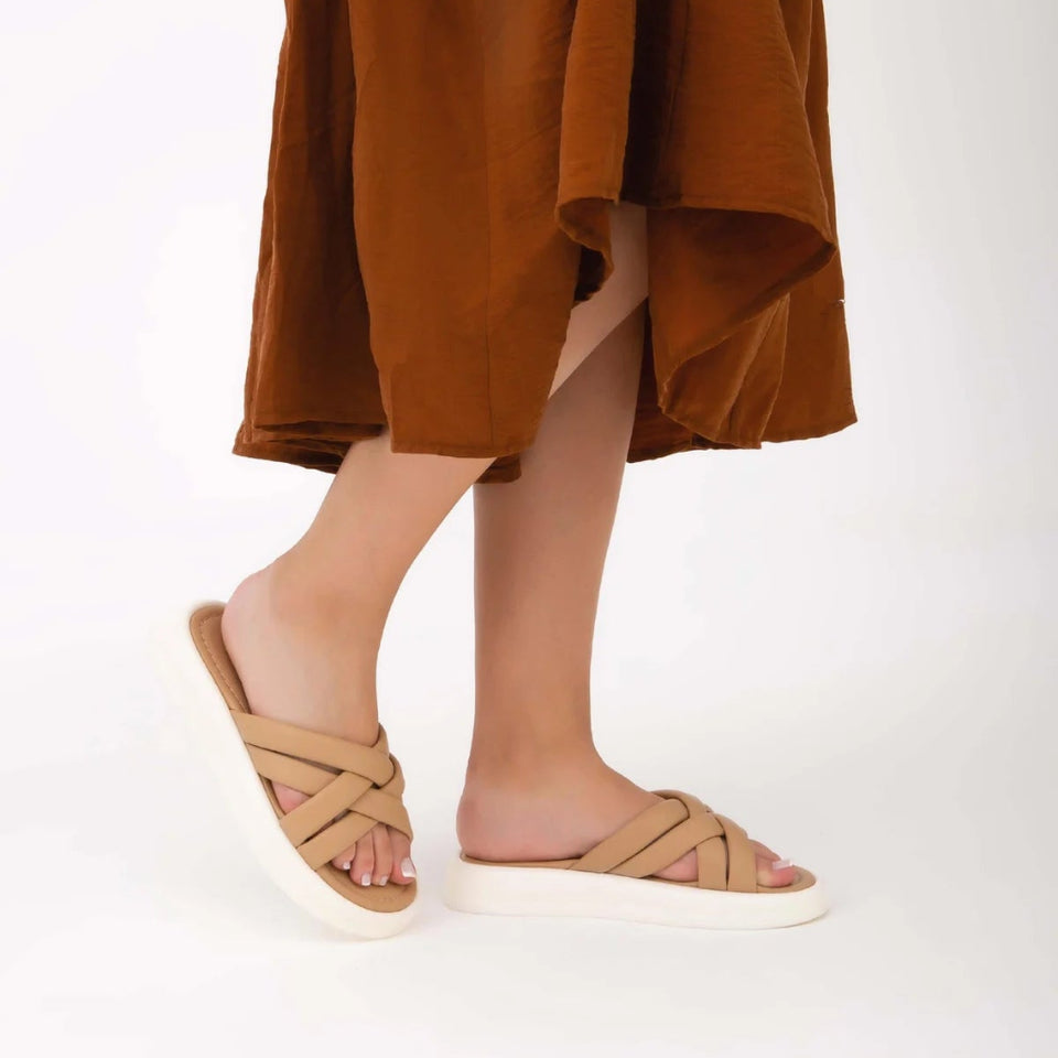 A person wearing a draped brown skirt and tan slide sandals with white soles, shown from the waist down against a plain white studio background.