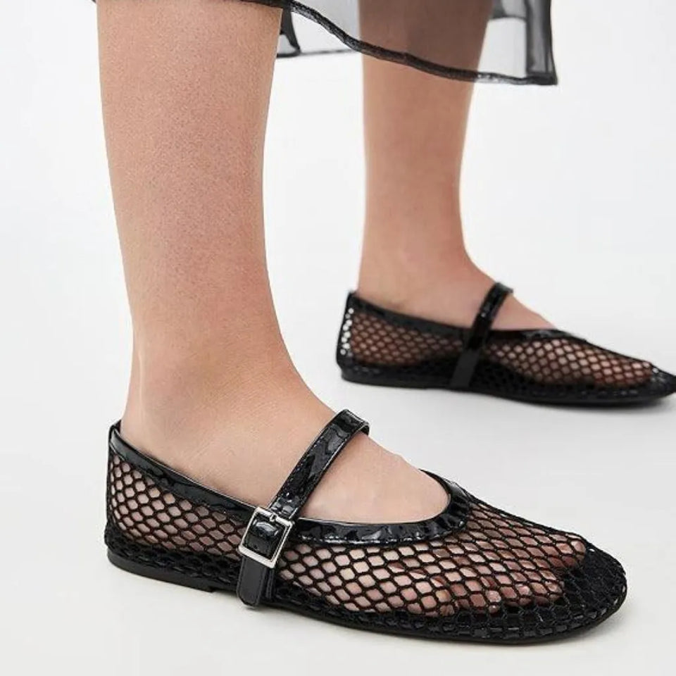 Black fishnet Mary Jane flats with a glossy strap and silver buckle, shown on a model's feet against a white background.