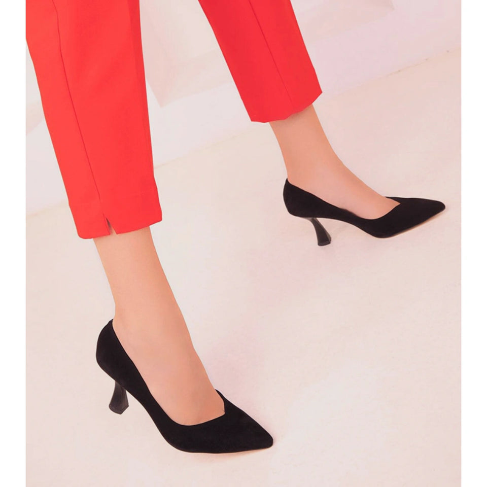 Black pointed-toe kitten heel pumps worn with bright red cropped trousers, shown on a model against a light pink studio background.