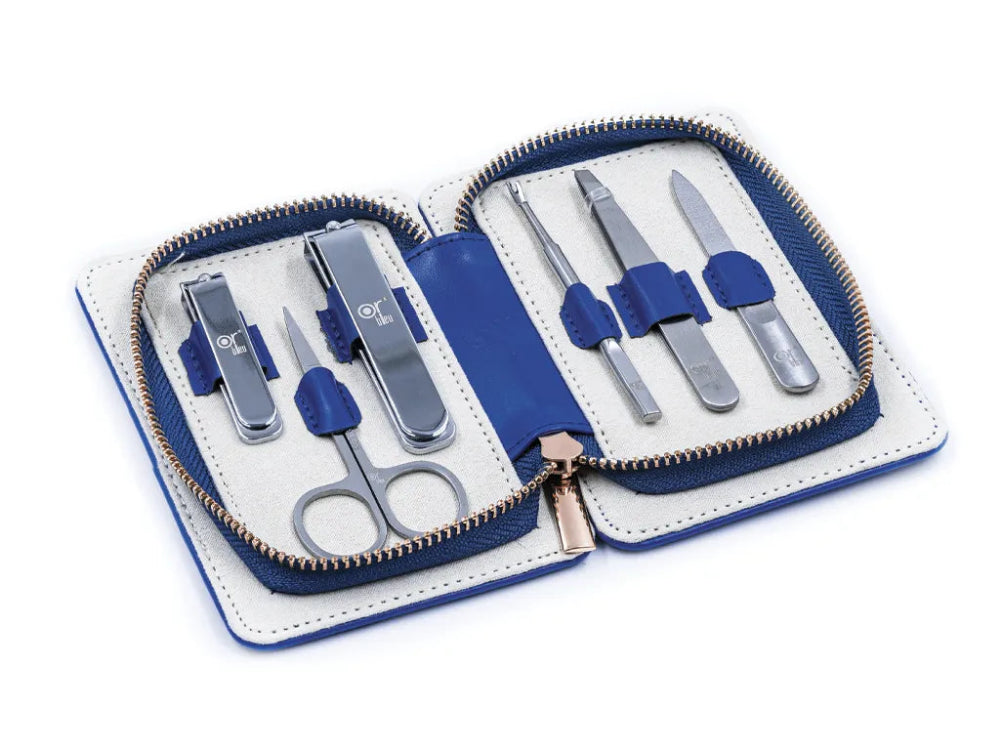 A manicure travel set by OR Bleu displayed open with various grooming tools like nail clippers, a nail file, and cuticle pusher arranged neatly. The set is contained in a blue synthetic leather case.