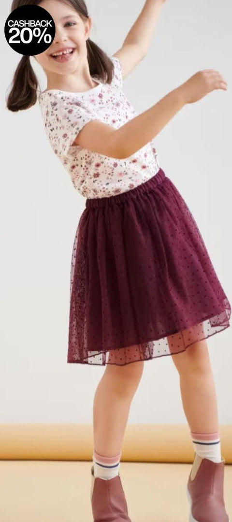 Young girl in a floral top and burgundy skirt standing on a light background