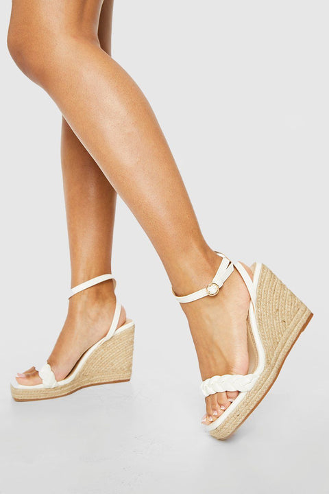 White wedge sandals with jute sole worn by a person on a light gray background