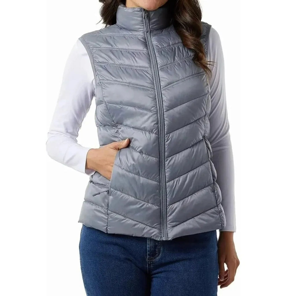 A woman wearing a gray zip-front puffer vest over a white long-sleeve shirt and blue jeans, shown against a plain white studio background.