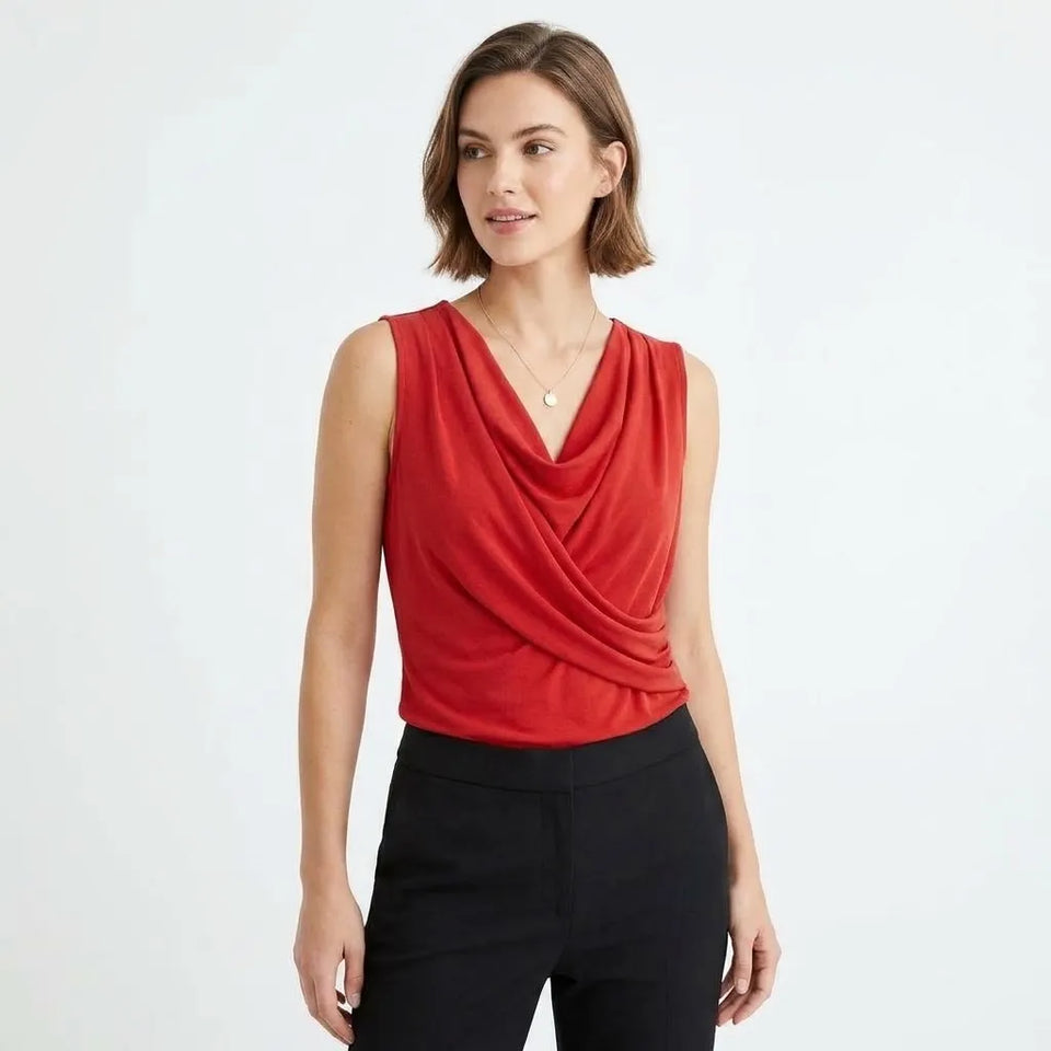 A woman modeling a sleeveless red draped top with black pants against a plain white studio background.