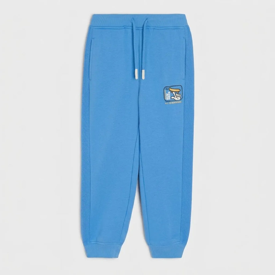 A pair of bright blue sweatpants with a drawstring waist and a small embroidered patch on the left thigh, shown against a light gray background.