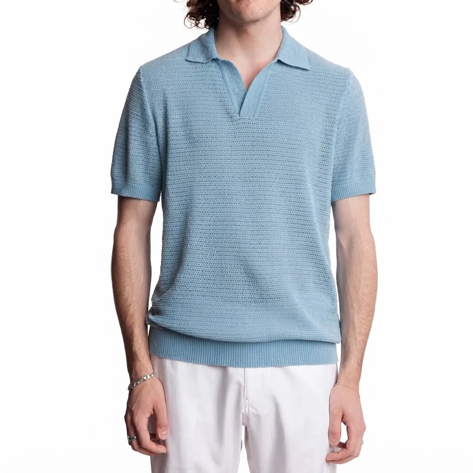 A man wearing a light blue textured short-sleeve polo shirt and white pants, shown from the waist up against a plain white background.