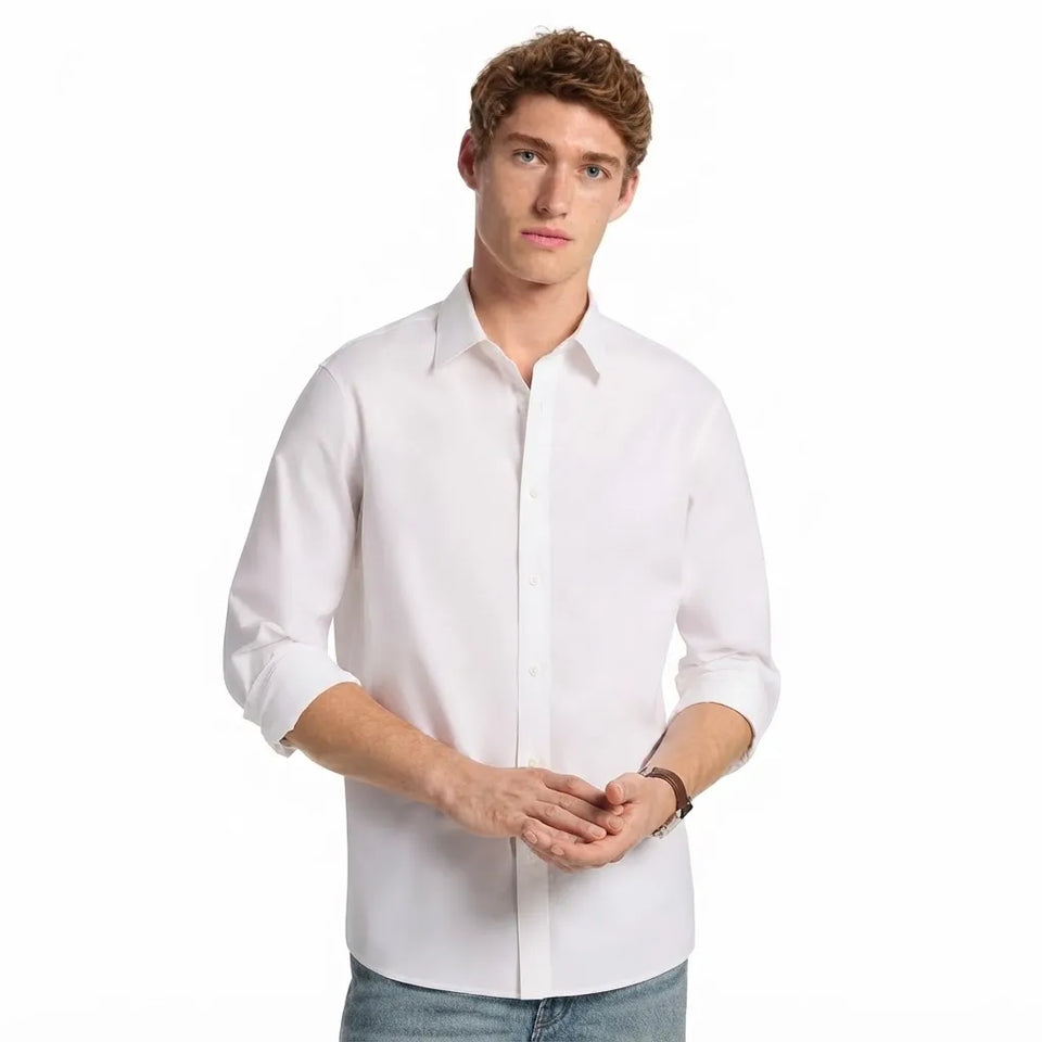 A man wearing a white long-sleeve button-down shirt with rolled-up sleeves and light blue jeans, standing against a plain white background.