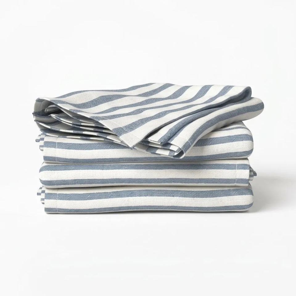 A stack of folded striped fabric napkins or table linens in blue-gray and off-white, photographed on a clean white studio background.