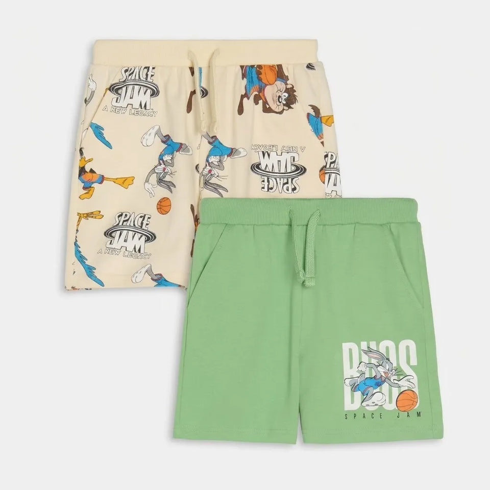Two pairs of kids' Space Jam themed lounge shorts, one in beige with a multicolor cartoon print and one in light green with a large Space Jam logo graphic, displayed on a light gray background.
