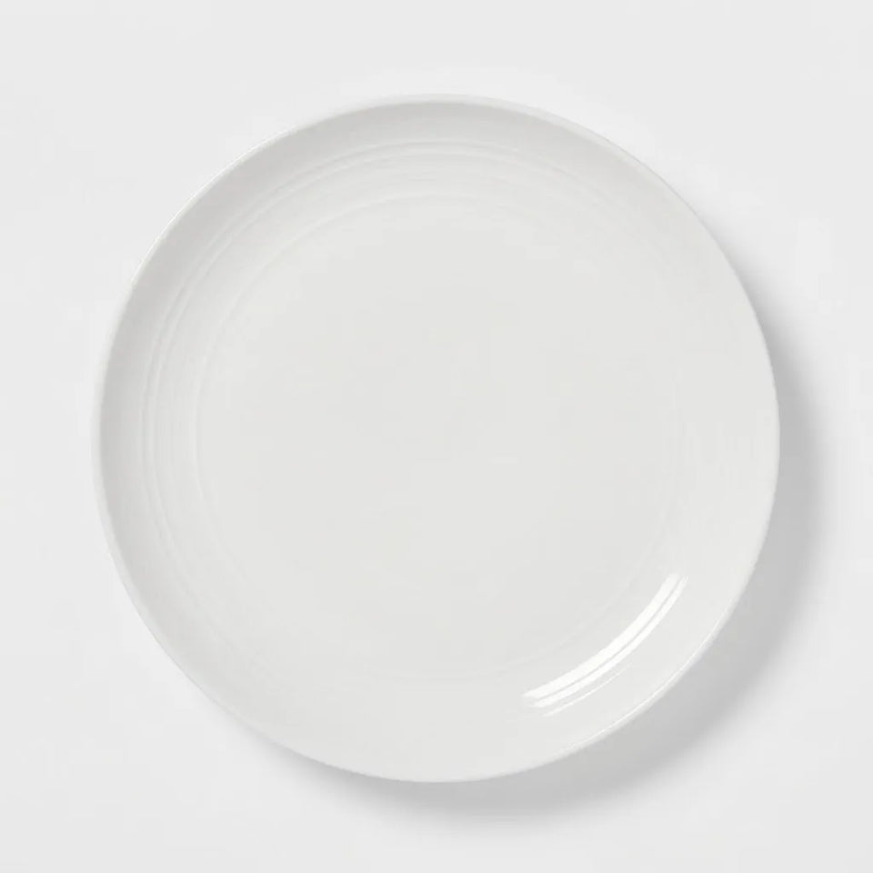 A minimalist white ceramic plate with subtle concentric ring details, photographed from directly above on a clean white background.