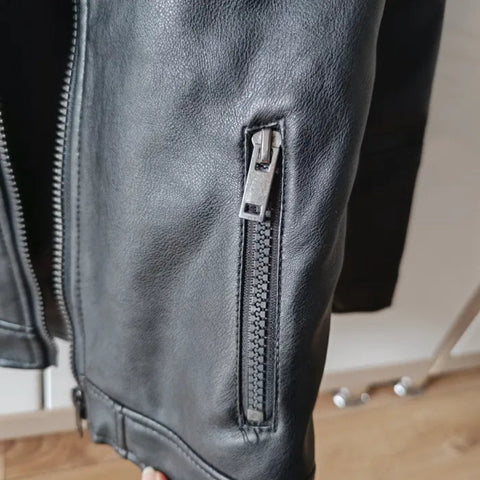 Close-up of a black leather jacket with a zipper on a wooden floor.